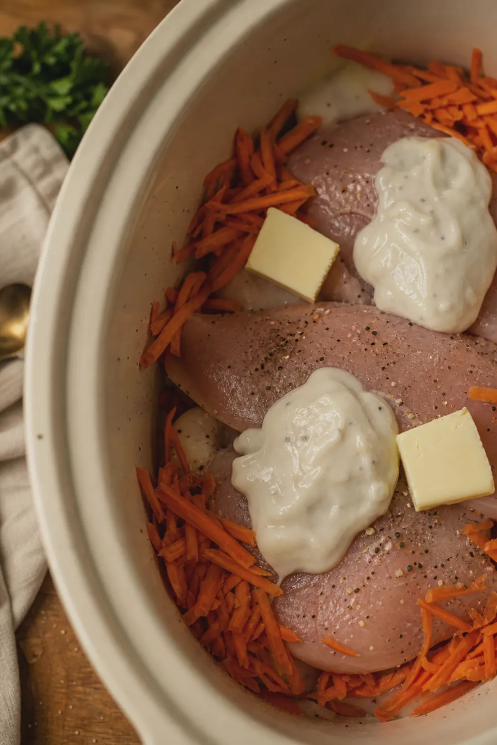 Raw chicken breasts layered with cream of chicken soup, butter slices, and seasonings in a slow cooker crock before cooking