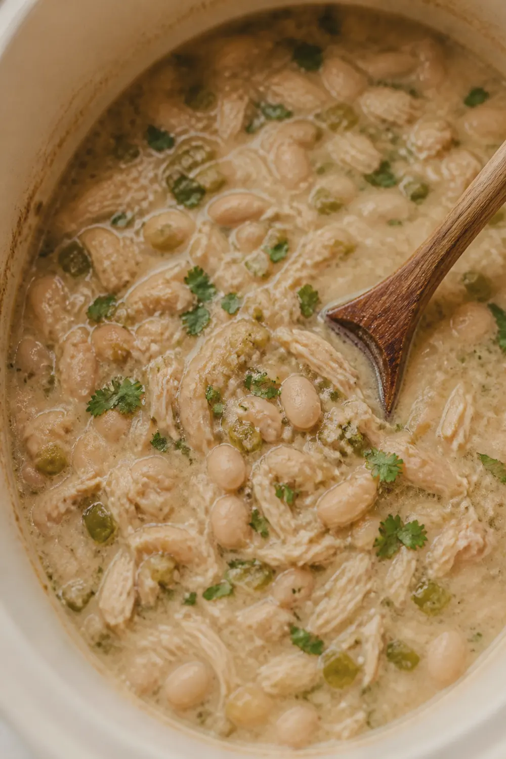 Finished creamy white chicken chili in the slow cooker with melted cream cheese, shredded chicken, and fresh cilantro stirred through